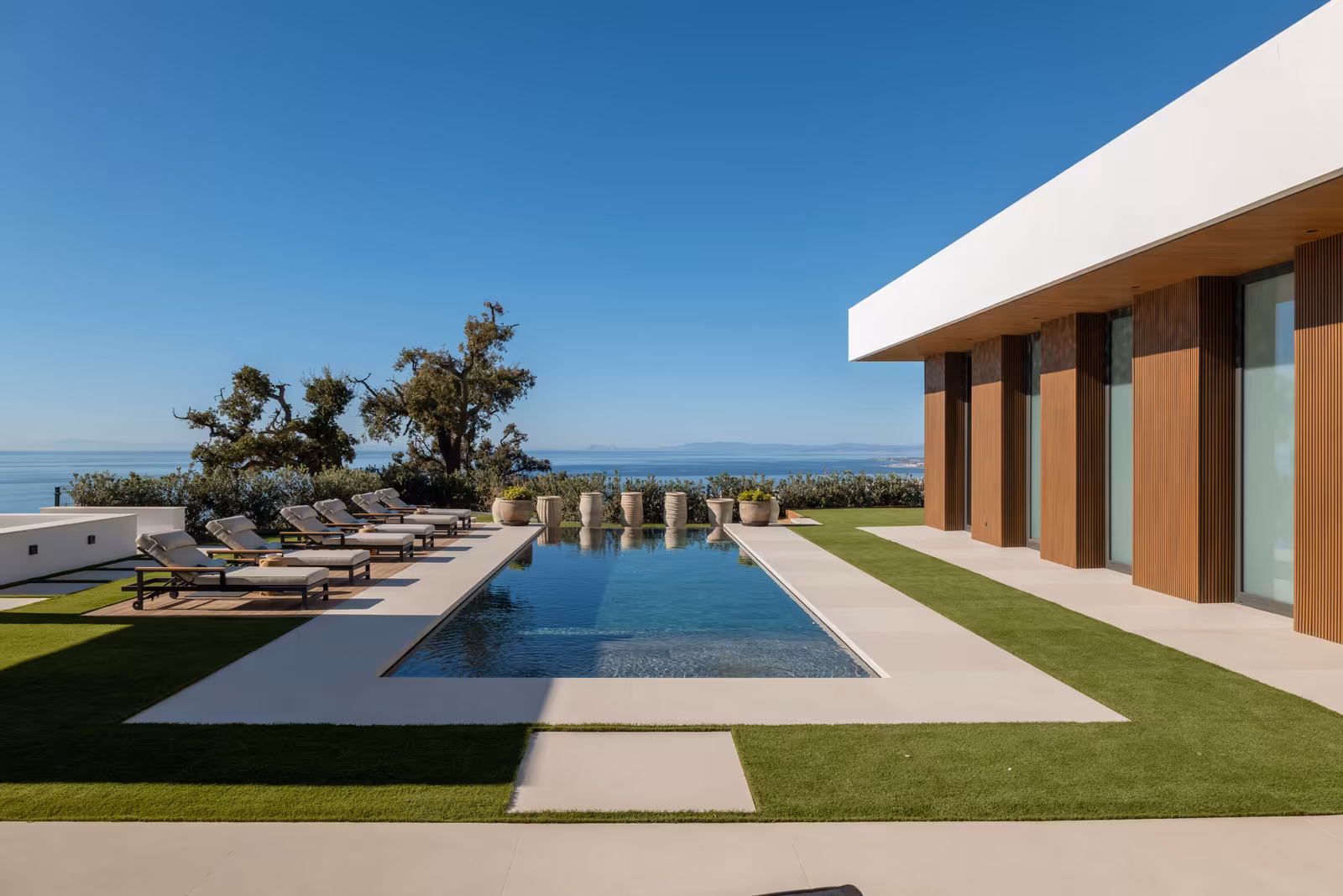 The House: long pool and timber-toned elevations with the sea beyond
